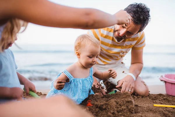 Familia joven con niños pequeños jugando en la playa en vacaciones de verano . —  Fotos de Stock