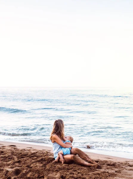 Ibu muda menyusui putri balita di pantai pada hari libur musim panas . — Stok Foto
