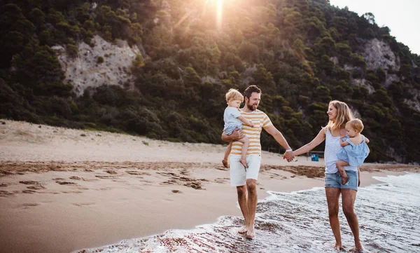 Una familia con dos niños pequeños caminando en la playa en vacaciones de verano al atardecer . — Foto de Stock