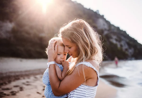 Jovem mãe com uma menina na praia em férias de verão ao pôr do sol . — Fotografia de Stock