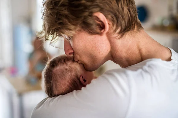 生まれたばかりの赤ちゃんを自宅で抱き、キスをする若い父親. — ストック写真
