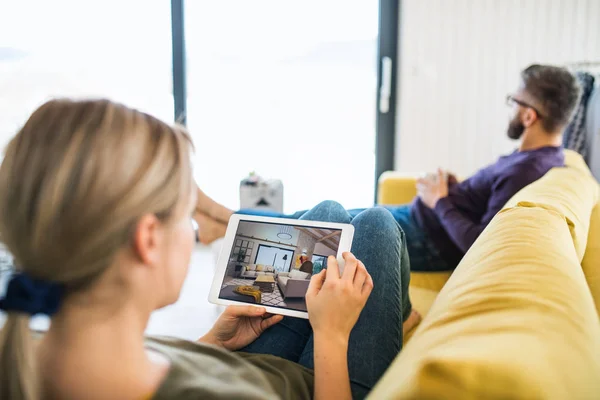 Pareja joven con la tableta sentada en el sofá, mirando bocetos de diseño de interiores . — Foto de Stock