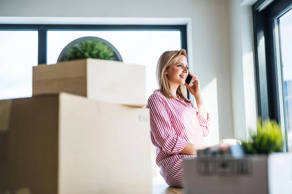 Una mujer joven con teléfono inteligente que se mueve en un nuevo hogar . — Foto de Stock