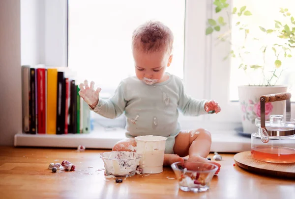 Een kleine rommelig peuter jongen zittend op keuken teller thuis, eten. — Stockfoto