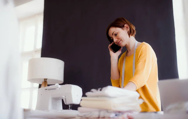 Mujer creativa joven en un estudio, usando un teléfono inteligente. Una puesta en marcha de negocio de sastrería . —  Fotos de Stock