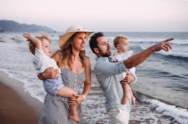 Una familia con dos niños pequeños caminando en la playa en vacaciones de verano al atardecer . — Foto de Stock