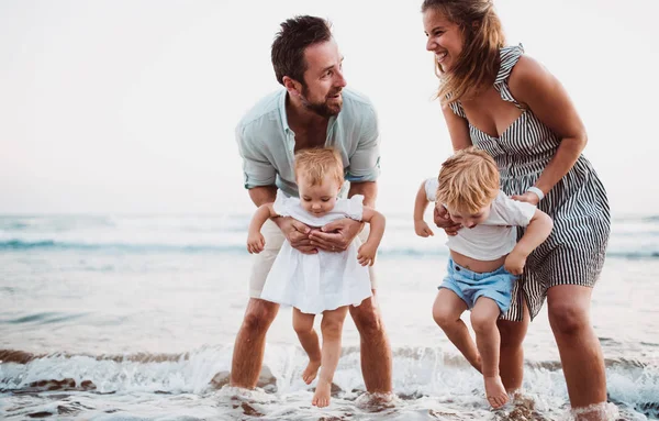 Una familia joven con dos niños pequeños divirtiéndose en la playa en las vacaciones de verano . —  Fotos de Stock