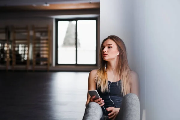 Spor salonunda kulaklıklı ve akıllı telefonu olan genç bir kız veya kadın. — Stok fotoğraf