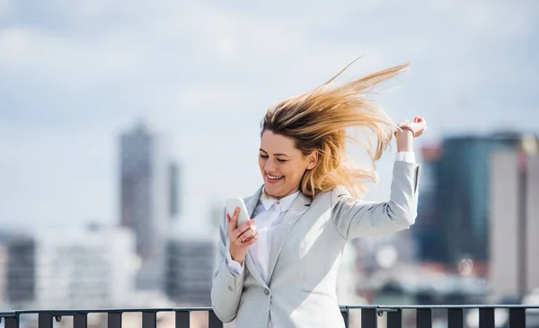 En ung affärs kvinna med smartphone stående på en terrass, uttrycker spänning. — Stockfoto