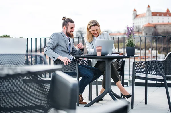 Deux jeunes hommes d'affaires avec ordinateur portable assis sur une terrasse à l'extérieur du bureau, travaillant . — Photo