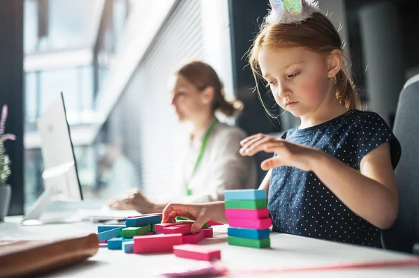 Une femme d'affaires avec une petite fille assise dans un bureau, travaillant et jouant . — Photo