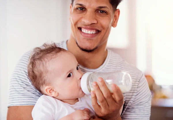 Un ritratto della bottiglia del padre che alimenta un piccolo figlio del bambino all'interno di casa . — Foto Stock