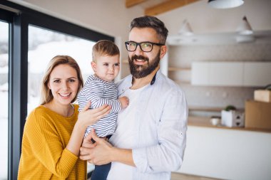 Yeni evinde hareketli bir yürümeye başlayan çocuk kızla genç aile portresi.