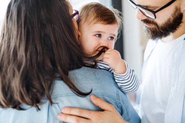 Evde, orta bölümde, evde duran ağlayan bir bebek kız ile genç bir aile.