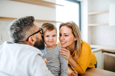 Genç bir ailenin portresi ve mutfakta bir bebek kız, öpüşme.