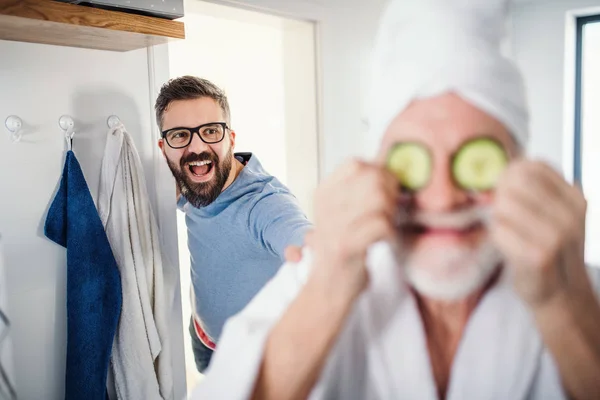 Ein erwachsener Hipster-Sohn und ein älterer Vater im Badezimmer zu Hause und haben Spaß. — Stockfoto