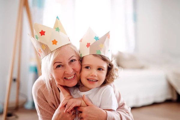 A portrait of small girl with grandmother hugging at home. — Stock Photo, Image