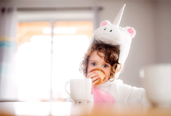 自宅のテーブルに座ってユニコーン マスクで小さな女の子の肖像画. — ストック写真