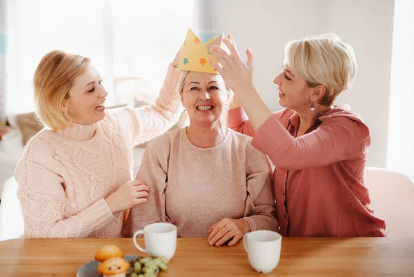 Evde masada oturan iki yetişkin kızı olan yaşlı bir anne, eğleniyor. — Stok fotoğraf