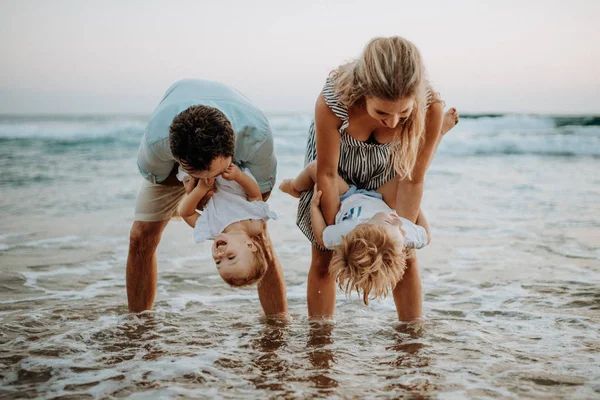 Une jeune famille avec deux enfants en bas âge qui s'amusent sur la plage pendant les vacances d'été . — Photo