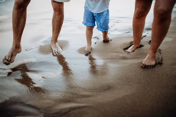 Sección media de padres con hija pequeña de pie en la playa en las vacaciones de verano . — Foto de Stock