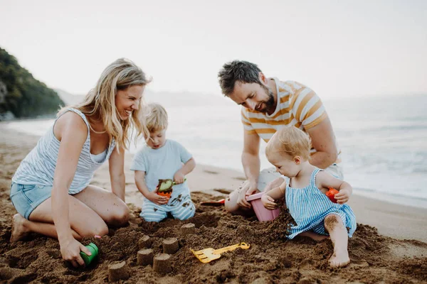 Jeune famille avec des enfants en bas âge jouant avec le sable sur la plage pendant les vacances d'été . — Photo