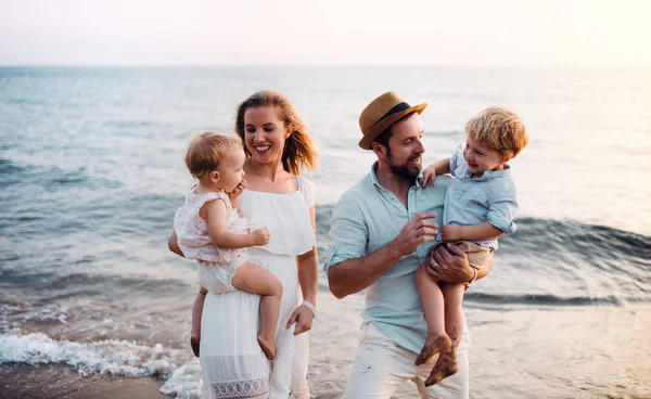 Familia joven con dos niños pequeños caminando en la playa en vacaciones de verano . — Foto de Stock