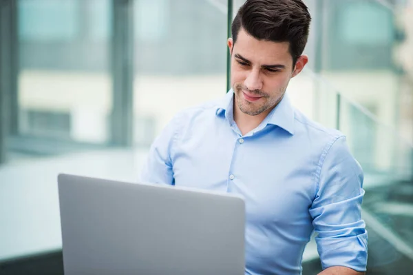 Een portret van jonge zakenman met laptop zittend in kantoor. — Stockfoto