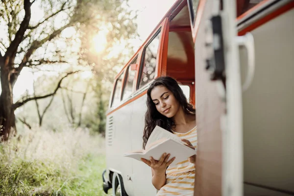 Uma jovem com um livro de carro em uma viagem pelo campo, lendo . — Fotografia de Stock