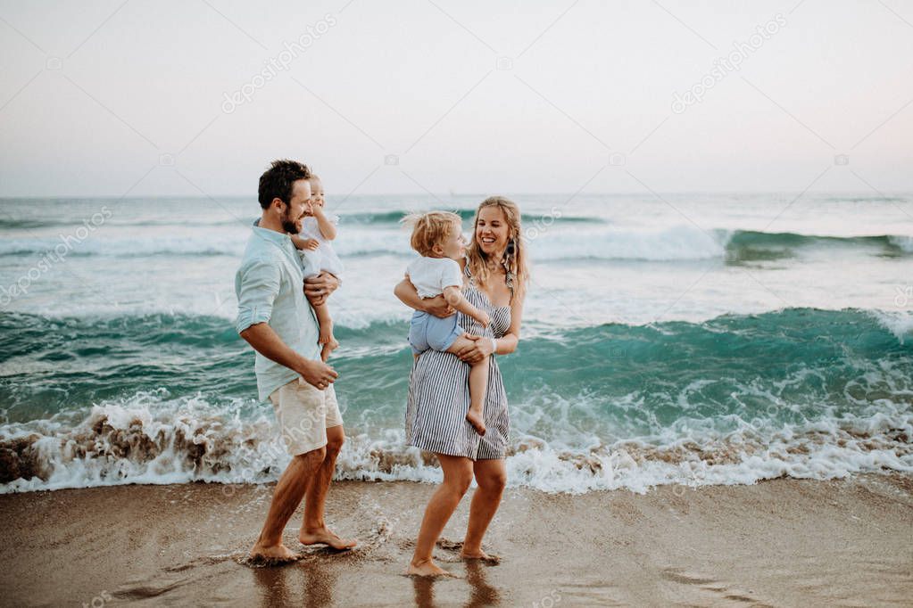 Young family with two toddler children walking on beach on summer holiday.