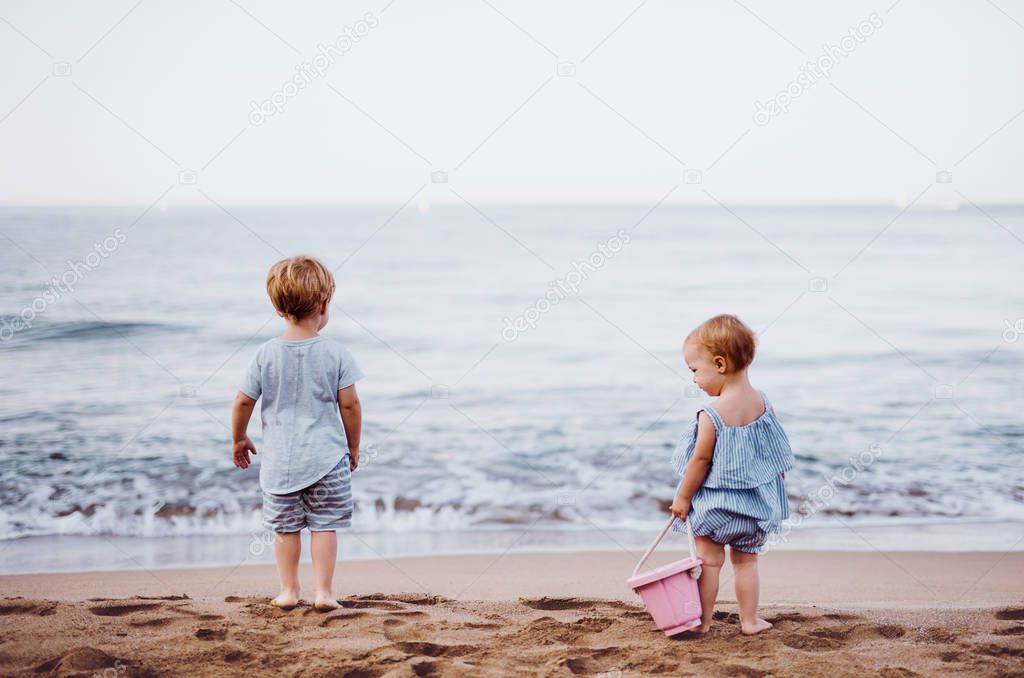 Two toddler children playing on sand beach on summer holiday.