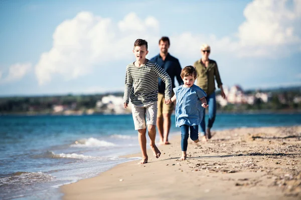 Familia joven con dos niños pequeños caminando al aire libre en la playa . — Foto de Stock