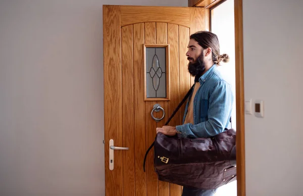 Jeune homme hipster avec sac entrant par la porte d'entrée en rentrant à la maison . — Photo