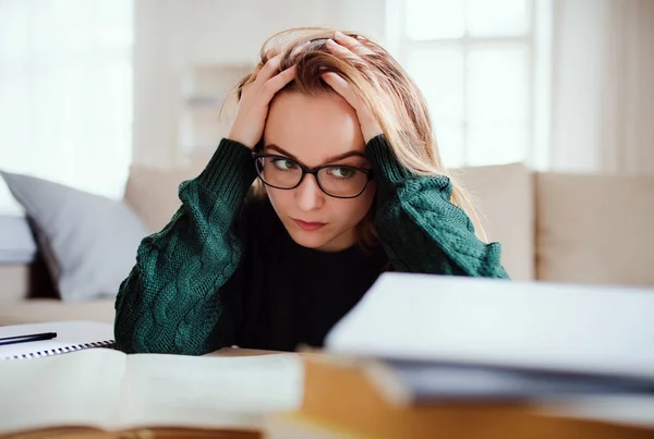 Uma jovem e triste estudante sentada à mesa, estudando . — Fotografia de Stock