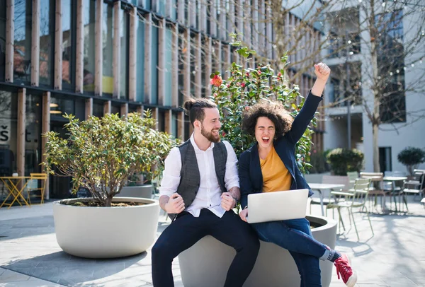 Young businesspeople with laptop outdoors in courtyard, expressing excitement. — Stock Photo, Image