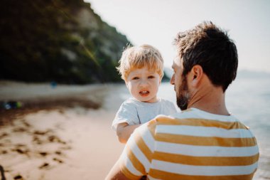 Yaz tatilinde sahilde duran bir bebek çocuk ile baba arka görünümü.