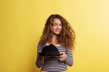 Sarı bir arka planda bir stüdyoda siyah şapka ile genç bir kadının portresi.