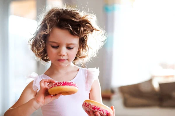 Uma menina pequena com donuts em casa . — Fotografia de Stock