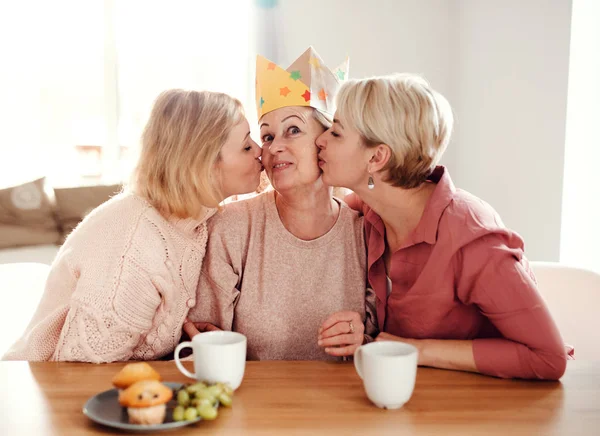 O mamă în vârstă cu două fiice adulte care stau la masă acasă, distrându-se . — Fotografie, imagine de stoc