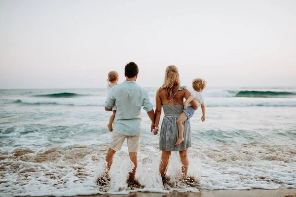 Una vista trasera de la familia con dos niños pequeños de pie en la playa en las vacaciones de verano . — Foto de Stock