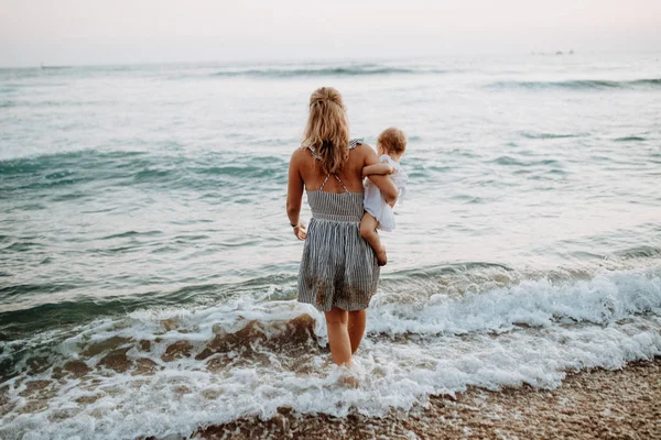 여름 휴가에 바다에서 걷는 유아 소녀와 함께 젊은 어머니의 뒷모습. — 스톡 사진