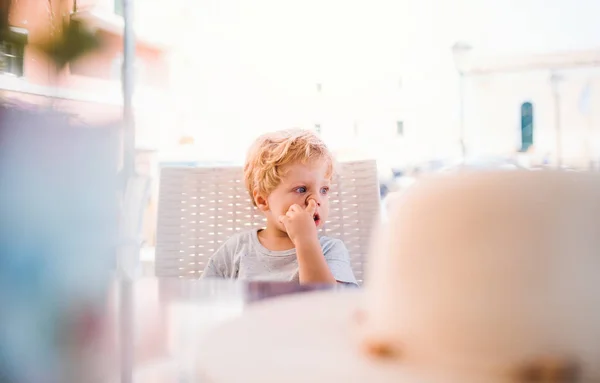 Piccolo ragazzo seduto in un ristorante all'aperto durante le vacanze estive, naso che scatta . — Foto Stock