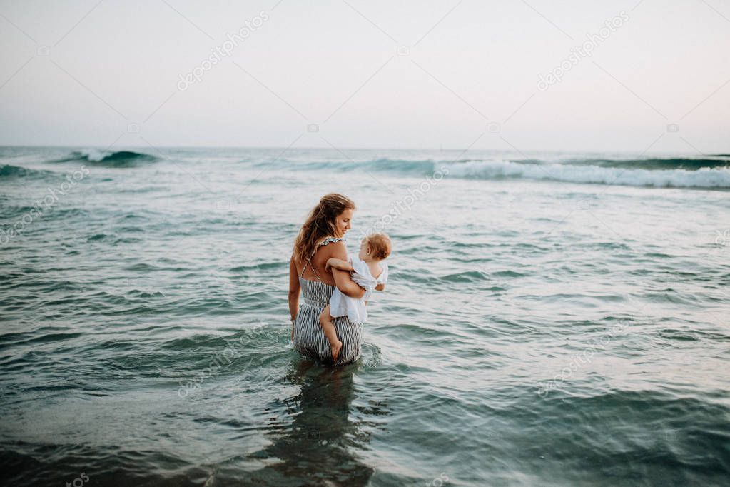 Rear view of young mother with a toddler girl walking in sea on summer holiday.