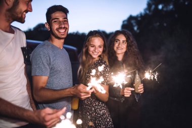 A group of friends with sparklers standing outdoors at dusk. clipart