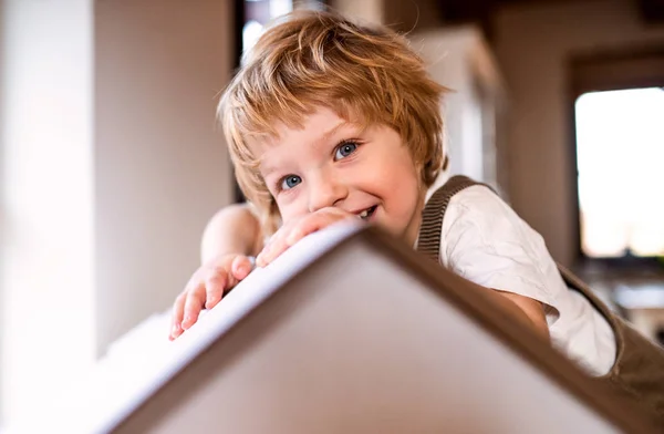 Ett småbarn pojke leker med en kartong papper hus inomhus hemma. — Stockfoto