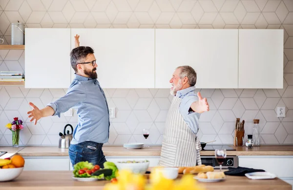 Adulte hipster fils et père aîné à l'intérieur dans la cuisine à la maison, en s'amusant . — Photo