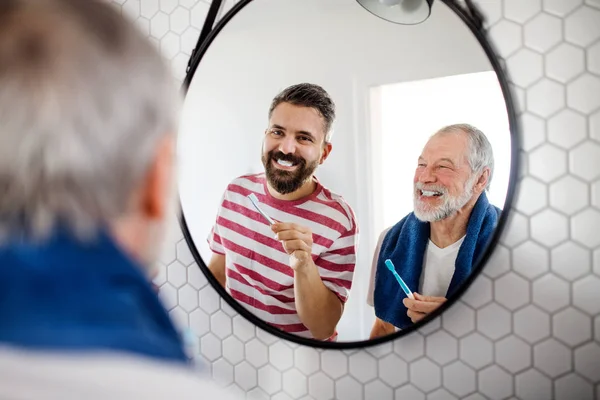 Un hijo hipster adulto y padre mayor en el baño en casa, cepillándose los dientes . — Foto de Stock