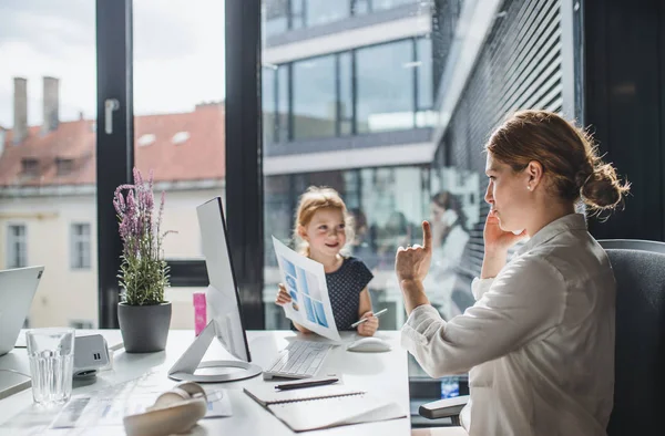 A businesswoman with small daughter sitting in an office, working. — Stock Photo, Image