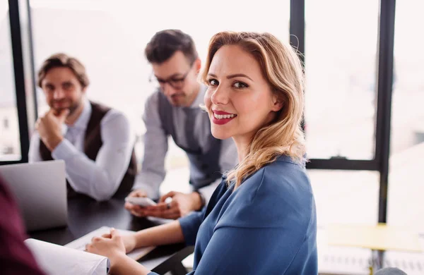 Een groep van jonge zakelijke mensen met laptop zittend in een kantoor, praten. — Stockfoto