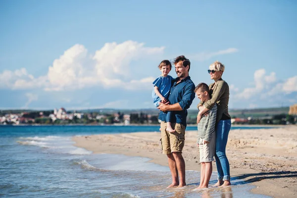 Νεαρή οικογένεια με δύο μικρά παιδιά να στέκονται έξω στην παραλία. — Φωτογραφία Αρχείου